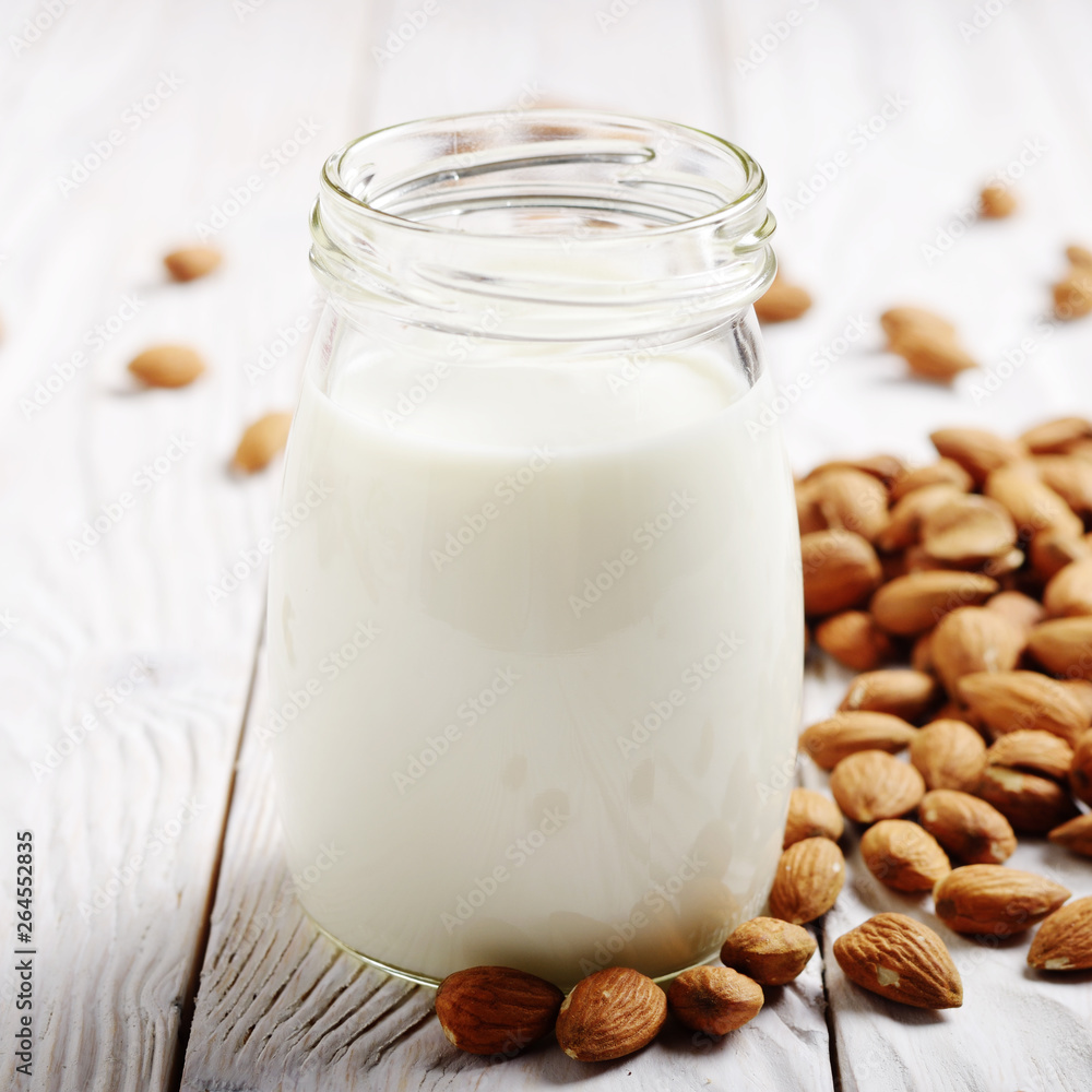 Milk or yogurt in mason jar on white wooden table with almonds aside Milk or yogurt in mason jar on white wooden table with almonds aside
