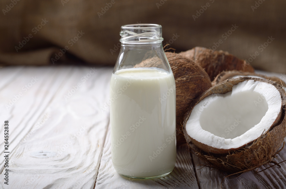 Milk or yogurt in glass bottle on white wooden table with coconut aside Milk or yogurt in glass bottle on white wooden table with coconut aside