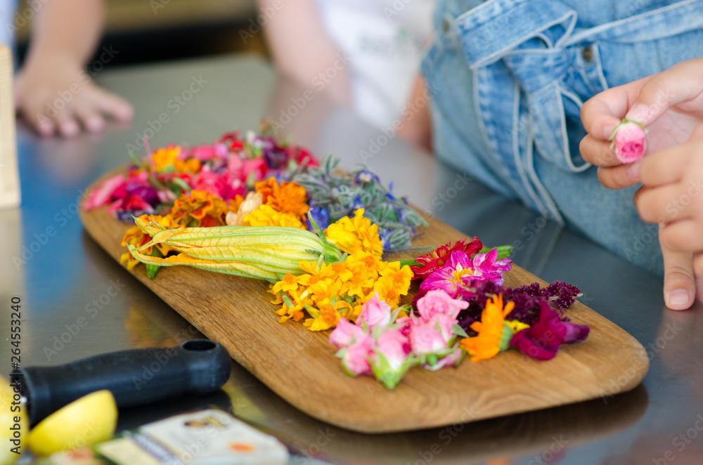 Cut edible flowers on a wooden cutting board. People are preparing to make dishes. It can be workshops for children and adults. Cut edible flowers on a wooden cutting board. People are preparing to make dishes. It can be workshops for children and adults.