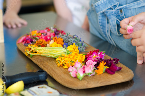 Cut edible flowers on a wooden cutting board. People are preparing to make dishes. It can be workshops for children and adults.