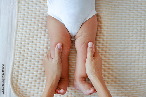 Mother hand massaging to leg of infant baby on the bed at home.