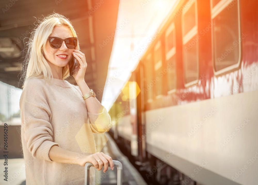 Fototapeta premium Blonde woman with her luggage stay and speak in her mobile near
