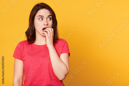 Half length front portrait of beautiful female isolated on yellow studio backgroud. Young emotional surprised woman standing with open mouth and covering it with fist. Human emotions concept.