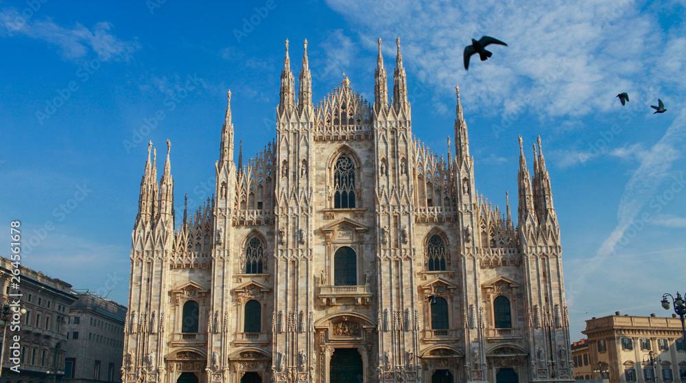 The cathedral of Milan with Gothic style of architecture and birds fly in the sky. Duomo di Milano in Italy