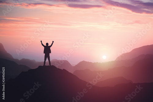 Victorious male person standing on mountain top with arms raised. Winning and success