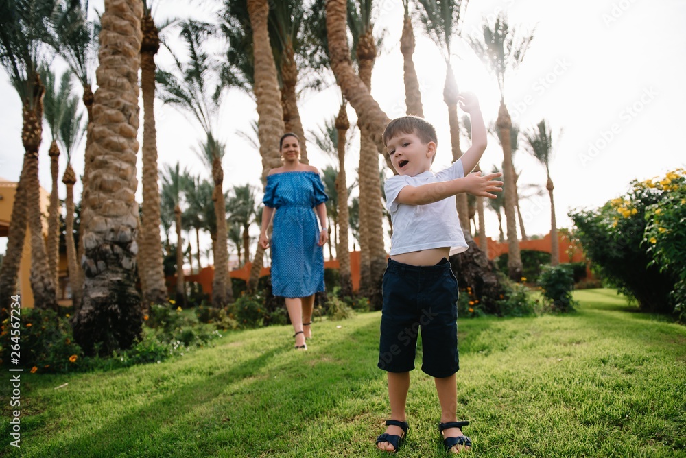 Obraz premium Stylish mother and handsome son having fun on a green lawn. Happy family concept. Beauty nature scene with family outdoor lifestyle. Happy family resting together. Mothers day