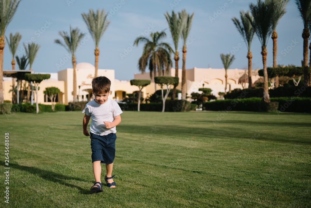 Cute boy runs on a green lawn playing catch-up in nature on a Sunny day.