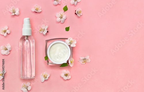 Cosmetic cream container, perfume bottle, deodorant and flowers apricot tree on coral living paper background with space for text. Top view, flat lay