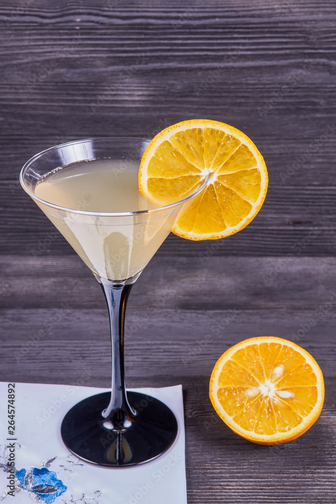 Glass of martini with fresh orange juice and orange slice, napkin and open orange, on a dark wooden background.