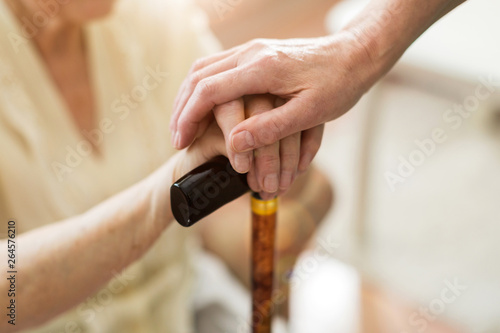 Close-up of woman holding senior's hands leaning on cane