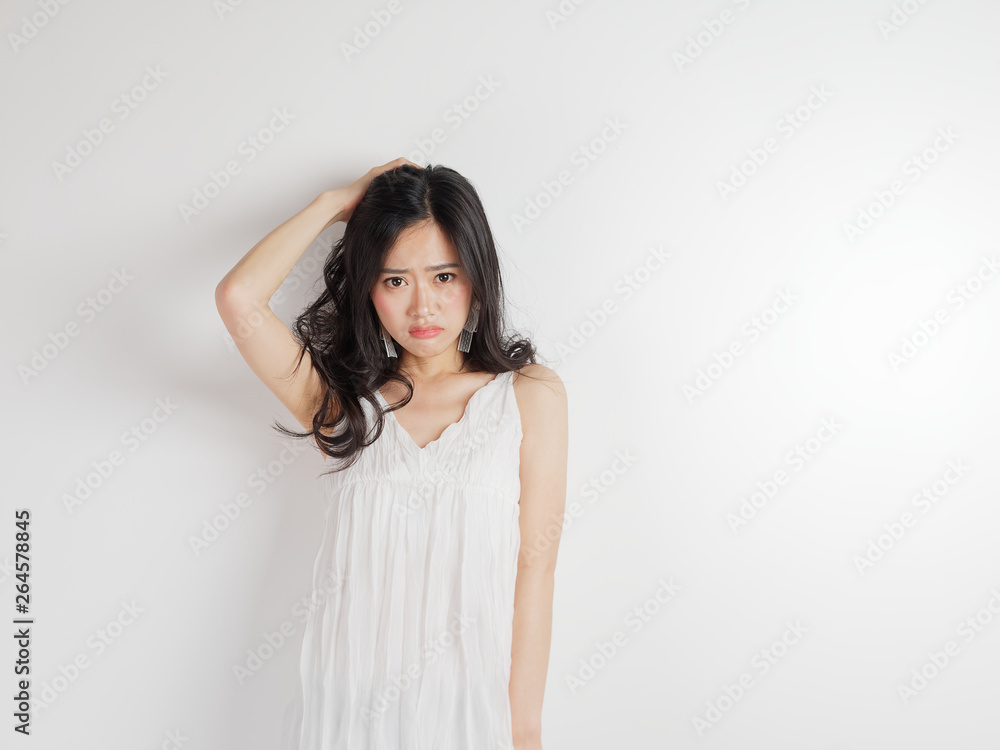 Portrait of beautiful Chinese woman in sexy white dress posing with white wall background, young girl puts her hand on head and looks unhappy. Portrait of beautiful Chinese woman in sexy white dress posing with white wall background, young girl puts her hand on head and looks unhappy.