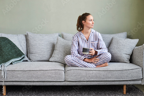 Pretty pajamas girl on sofa with morning coffee