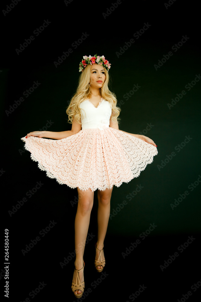 Fototapeta premium luxury sexy girl model blonde with big Breasts with a wreath of flowers on her head in a pink short dress isolated on a black background