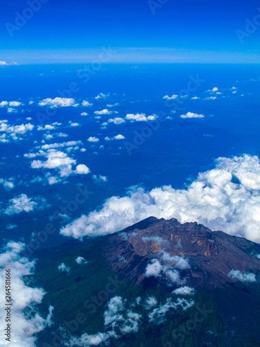 Inactive volcano in Indonesia with aerial view, surrounded by some clouds in a very bright blue sky day.