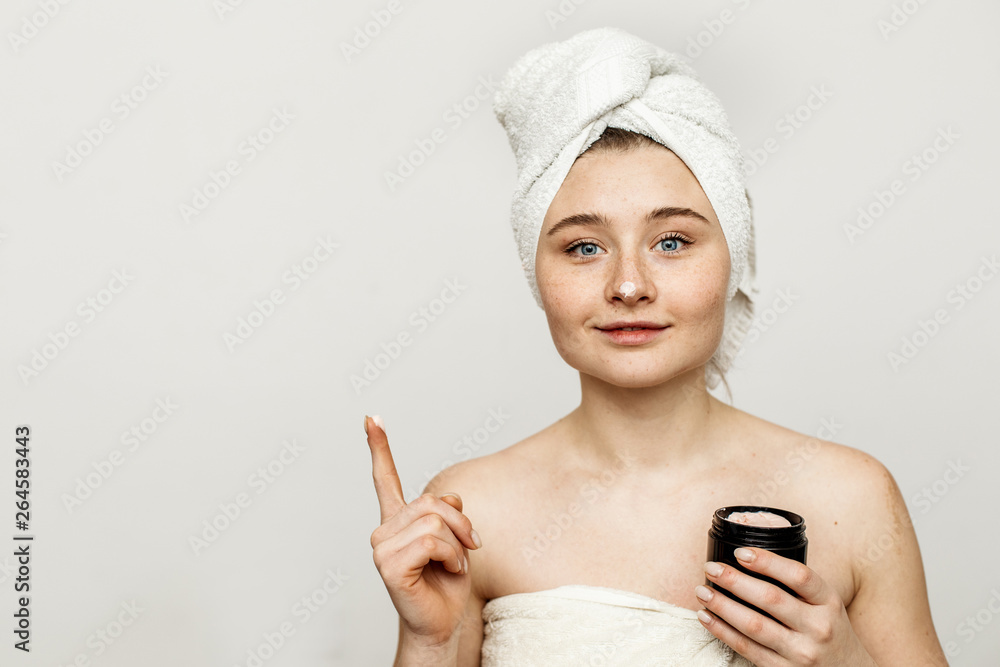 Nice young attractive woman hold face cream jar in hand. Face mask. Model after shower. White towel around hair and body. Isolated on grey background. Nice young attractive woman hold face cream jar in hand. Face mask. Model after shower. White towel around hair and body. Isolated on grey background.