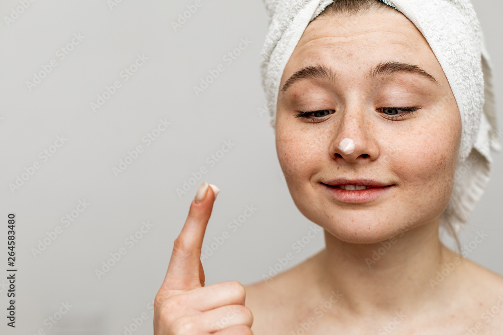 Portrait of nice young woman face. White cream spot on nose tip. Point with finger. Naked after shower. Isolated on grey background. Portrait of nice young woman face. White cream spot on nose tip. Point with finger. Naked after shower. Isolated on grey background.