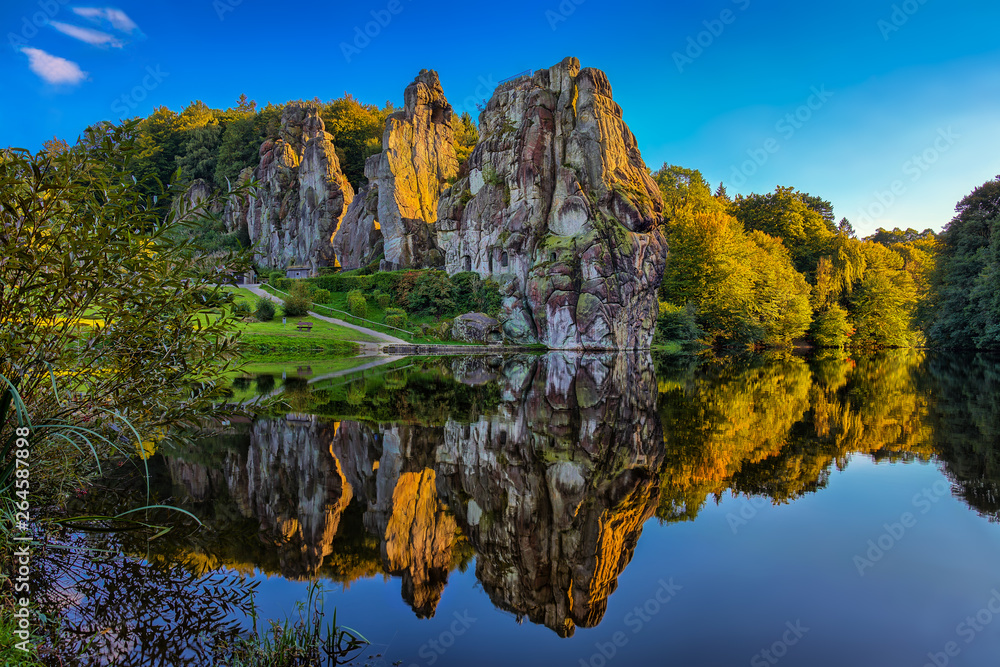 The Externsteine in the evening at sunset with the lake in the foreground and beautiful reflections in the water.