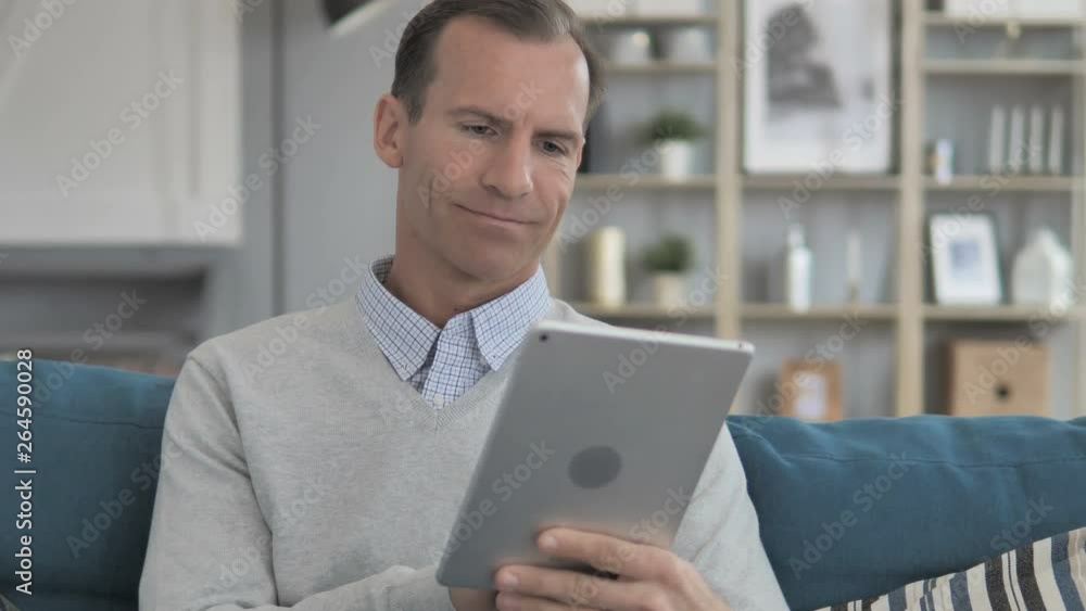 Middle Aged Man Using Tablet while Relaxing on Couch Middle Aged Man Using Tablet while Relaxing on Couch