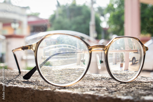 A pair pf round glasses on a rough surface under the sun in a garden.