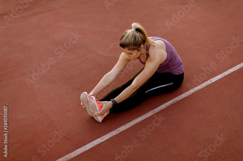 Young woman doing some exercises and streching legs at the court at outdoor