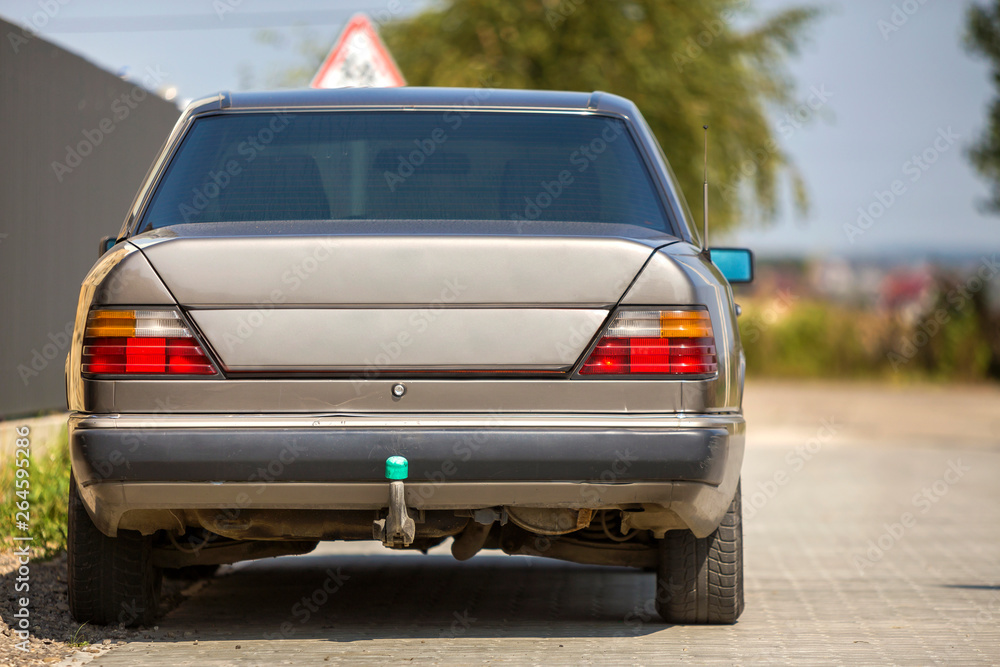 Back view of silver car parked on paved street in quiet area on sunny bright background. Transportation and urban parking concept. Back view of silver car parked on paved street in quiet area on sunny bright background. Transportation and urban parking concept.