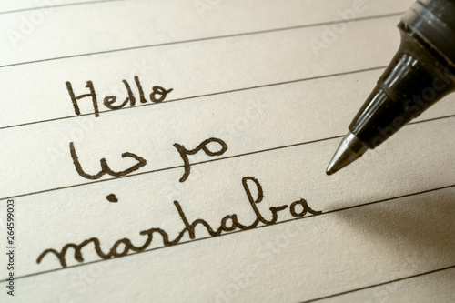 Beginner Arabic language learner writing Hello word Marhaba in abjad Arabic alphabet on a notebook photo