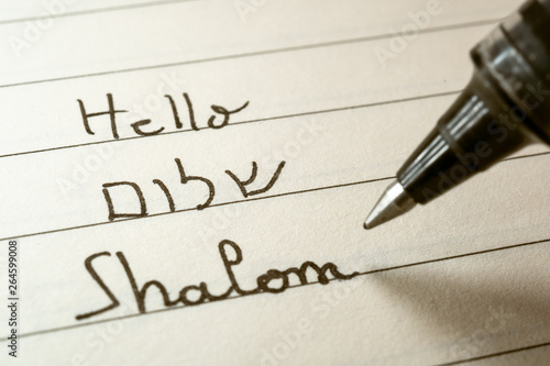 Beginner Hebrew language learner writing Hello Shalom word in Hebrew alphabet on a notebook photo