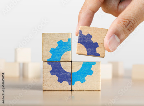 Hand putting the last piece of wooden blocks with the gear icon. Team work, unity, partnership or integration concept. photo