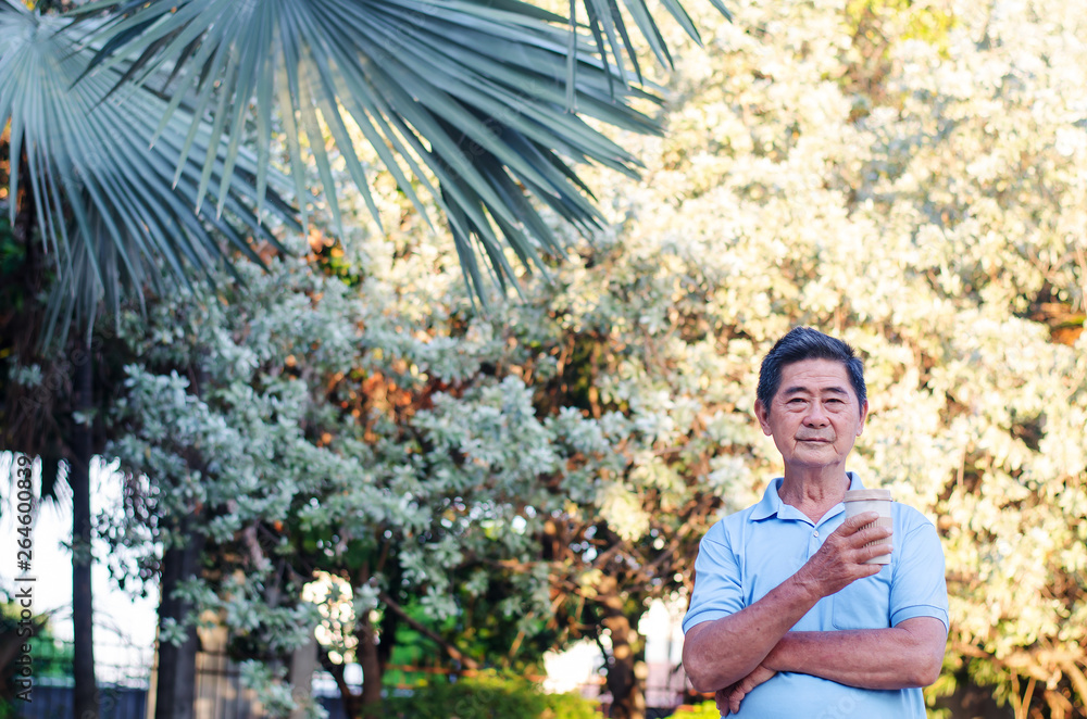 Asian senior gentleman standing in park and drinking coffee with relaxing on a sunny day