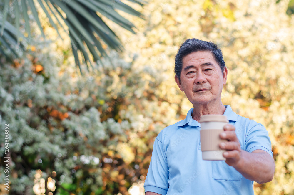 Asian senior gentleman standing in park and Hand holding take away coffee cup on a sunny day Asian senior gentleman standing in park and Hand holding take away coffee cup on a sunny day