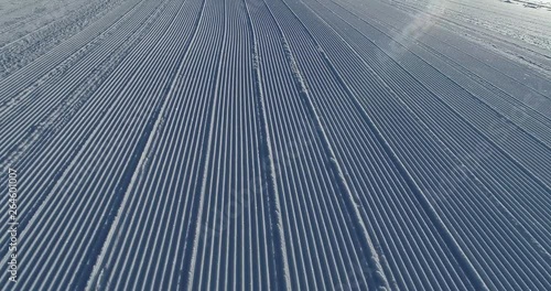 Flying over the ski slope on a frosty sunny day. Ski velvet, snow sparkles. Smooth parallel lines texture. 4K drone footage