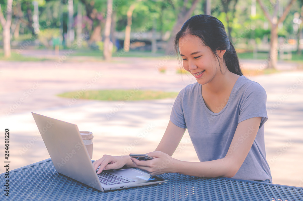 Young girl is a university student with cup of coffee and a phone in her hands working on a laptop at the table in the park. The concept of shopping online in the Internet Young girl is a university student with cup of coffee and a phone in her hands working on a laptop at the table in the park. The concept of shopping online in the Internet