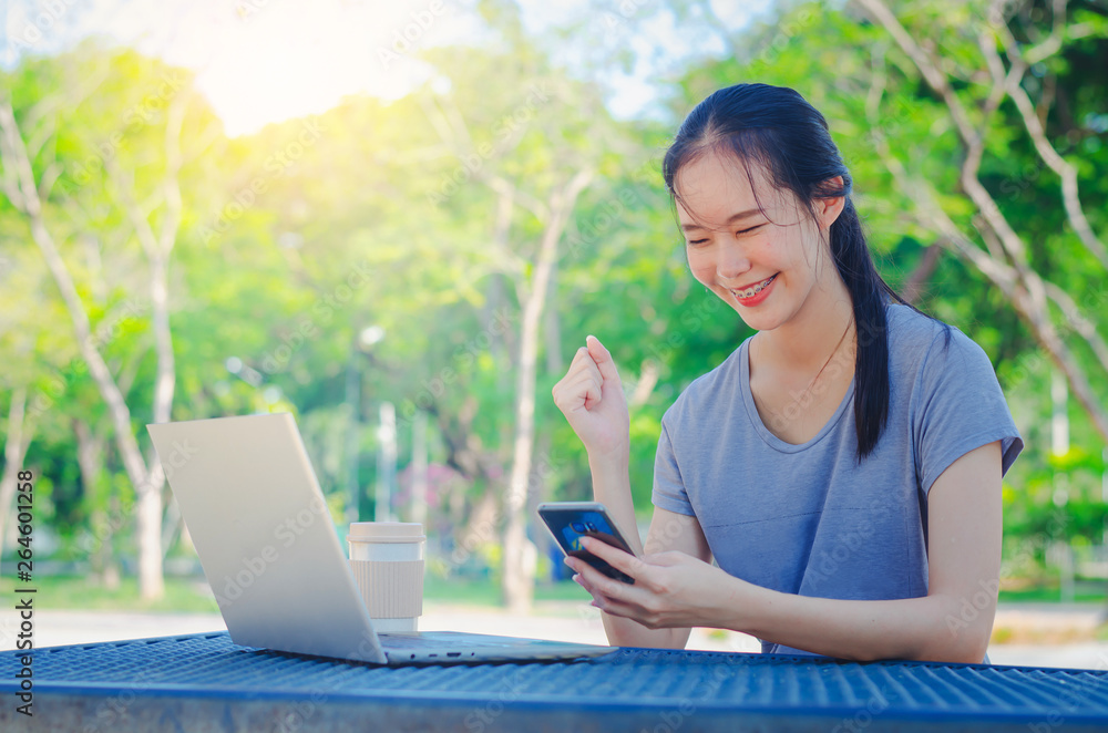 Successful young girl is a university student with cup of coffee and a phone in her hands working on a laptop at the table in the park. The concept of shopping online in the Internet Successful young girl is a university student with cup of coffee and a phone in her hands working on a laptop at the table in the park. The concept of shopping online in the Internet