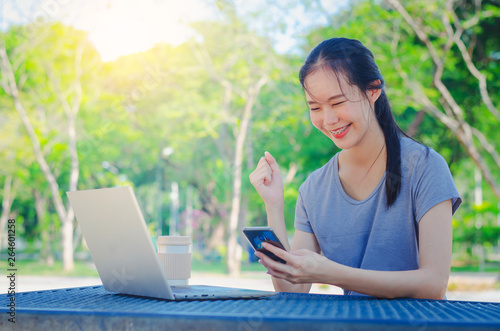 Successful young girl is a university student with cup of coffee and a phone in her hands working on a laptop at the table in the park. The concept of shopping online in the Internet