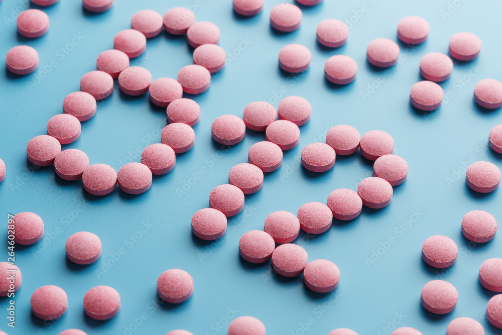 Pink pills in the shape of the letter B12 on a blue background, spilled out of a white can.