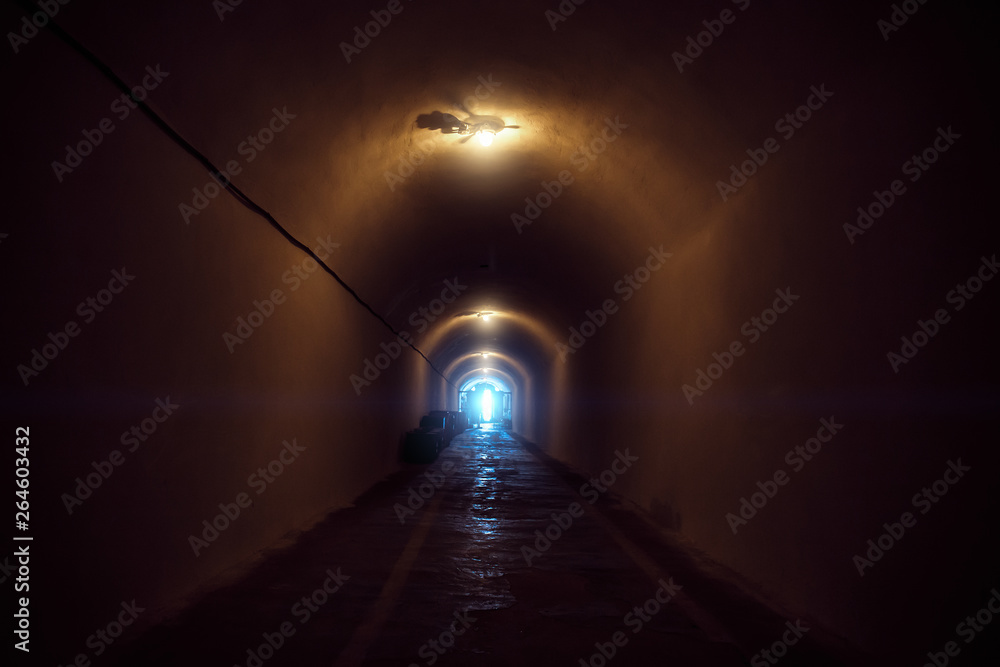 Underground dark tunnel with lamp illumination and blue light in end
