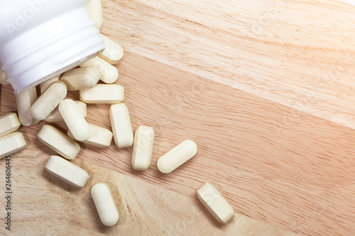 Pills poured out of a white bottle.Placed on light wood floor.Focus on tablets.