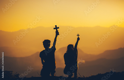 Two people sitting holding christian cross for worshipping God at sunset background. christian silhouette concept.