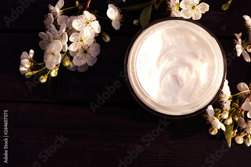 Eco cream in round tuba on black ooden background with white flowers. View from above. Place for text.