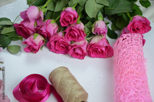 Florist at work: pretty woman making summer bouquet of roses on a working table. Kraft paper, scissors, envelope for congratulations on the table. View from above. Flat lay composition. photo