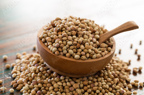 Organic Dried coriander seeds in wooden bowl with spoon on colored rustic background.