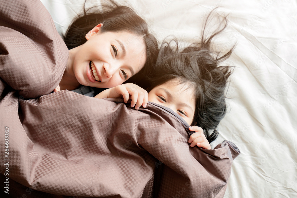 Obraz premium happiness asian family moment mom and daughter play and laydown with blanket on white bed home interior background