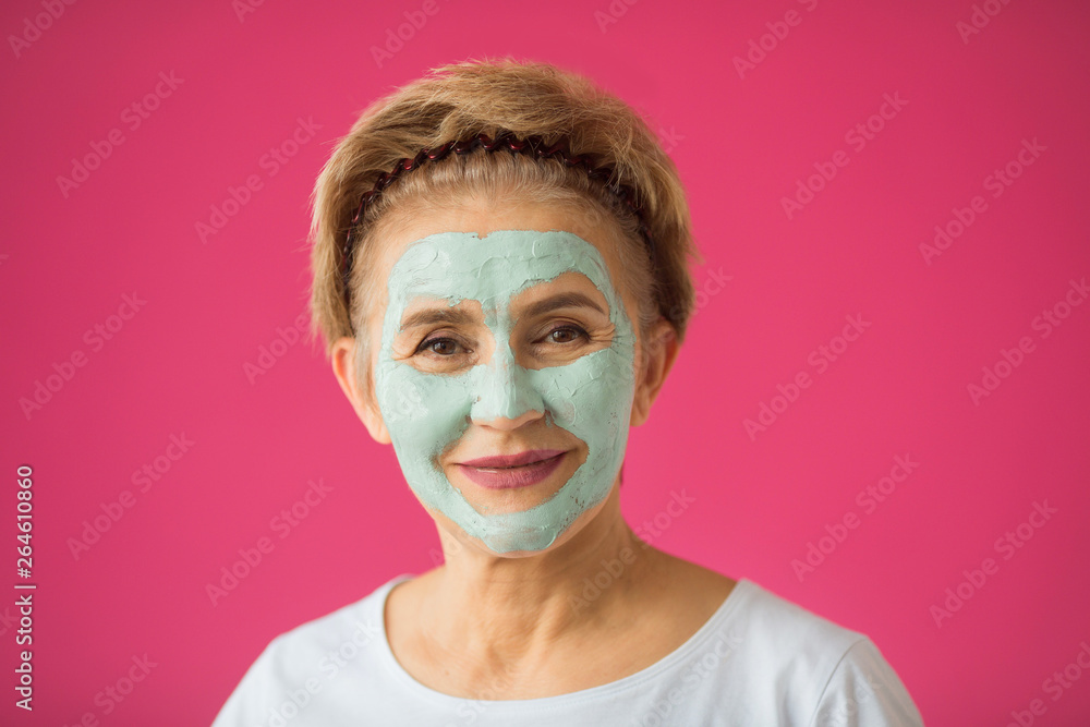 beautiful elderly woman with a wellness cream face mask on a pink background