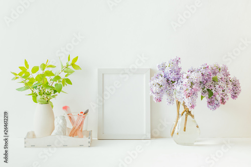 Home interior with decor elements. White frame, branches of lilac in a vase, cosmetic set