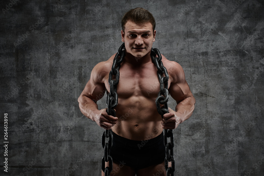 The concept of overcoming your weakness. Muscular pumped bodybuilder on black background. Sexy athlete man with huge chain around his neck