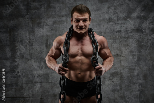 The concept of overcoming your weakness. Muscular pumped bodybuilder on black background. Sexy athlete man with huge chain around his neck