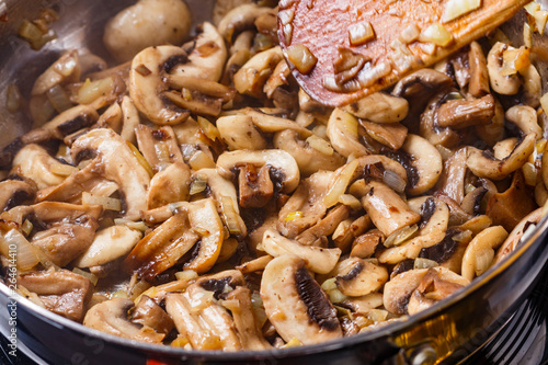 young woman in a gray apron roasts mushrooms in a frying pan