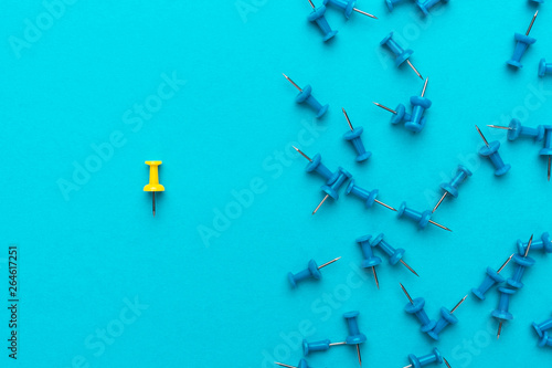 yellow push pin out of the crowd concept over blue backgound photo