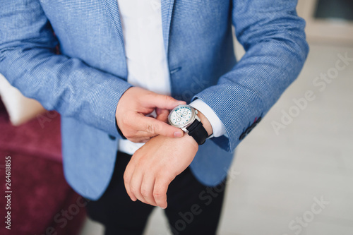 A businessman in a blue jacket adjusts his watch and checks the time. Wedding portrait. Morning groom and details. Work and business.