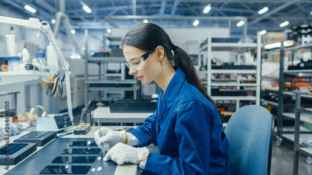 Young Female in Blue Work Coat is Assembling Printed Circuit Boards for Smartphones. Electronics Factory Workers in a High Tech Factory Facility.